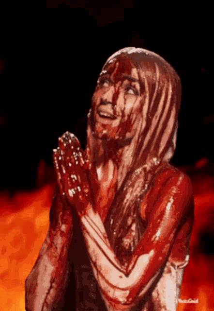 a woman covered in blood is praying with her hands together