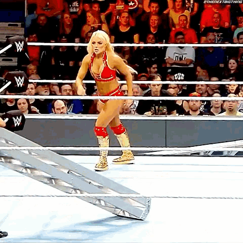 a female wrestler in a red and gold outfit is walking down a ramp in a wrestling ring .