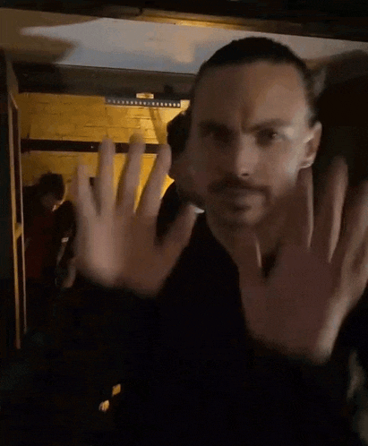 a man with a mustache is waving his hand in front of his face