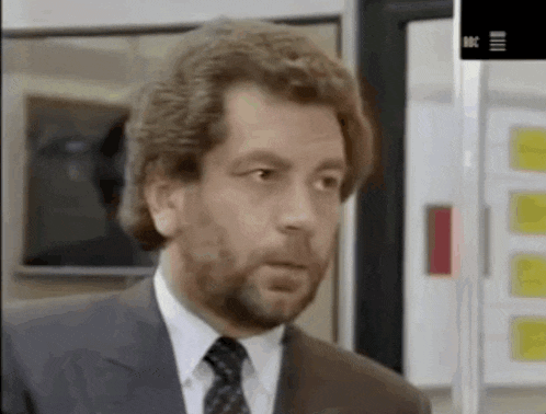 a man with a beard wearing a suit and tie looks at the camera