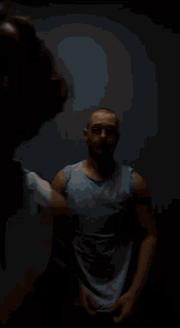 a man in a blue tank top stands in front of a dark background