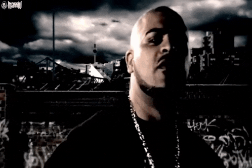 a bald man with a chain around his neck is standing in front of a city