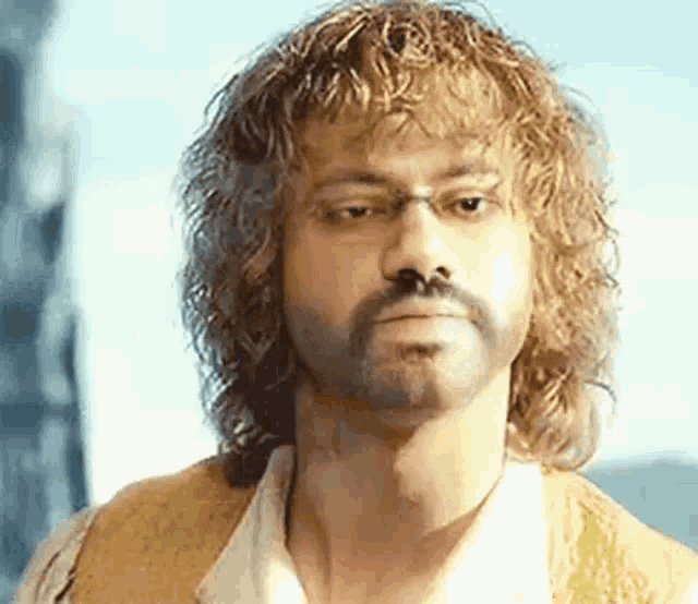 a man with curly hair and a beard is wearing glasses and a vest .