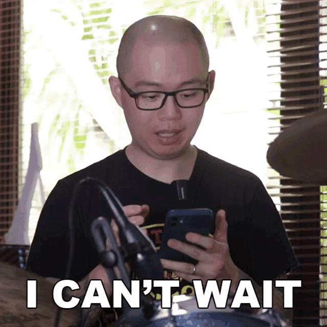 a bald man with glasses is looking at his phone and says i can 't wait