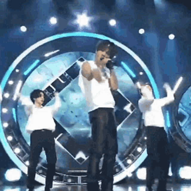 a man is singing into a microphone on a stage with two other men dancing behind him .