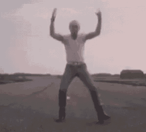 a man in a white shirt and jeans is dancing on a road with his arms in the air .