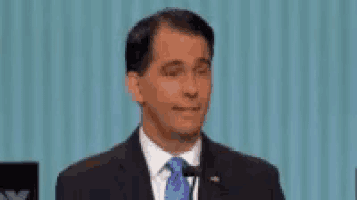 a man in a suit and tie is standing in front of a microphone and smiling .