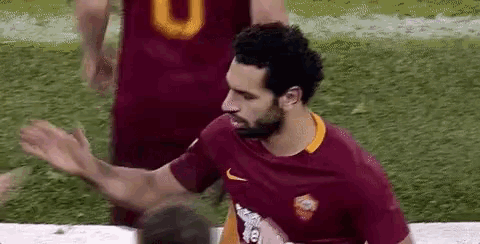 a soccer player in a maroon shirt is waving his hand while playing soccer .