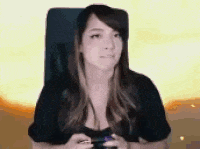 a woman is sitting in a chair holding a video game controller and looking at the camera .