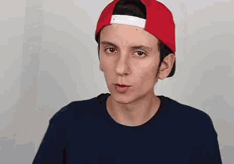 a young man wearing a red hat and a blue t-shirt is making a funny face .
