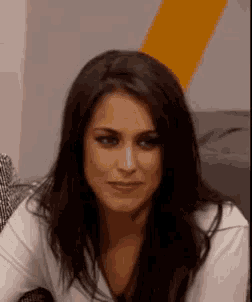 a woman with long dark hair and a white shirt is sitting on a couch .