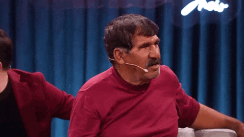 a man in a red shirt with a mustache is sitting on a couch .