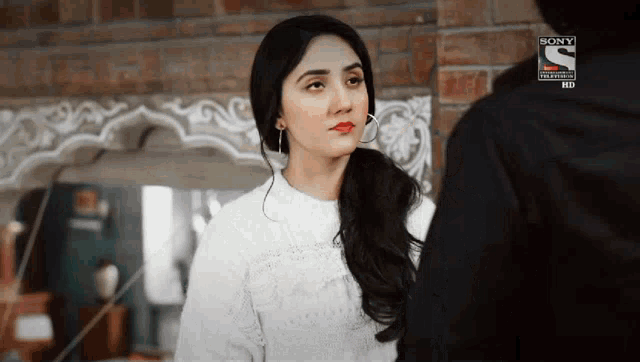 a woman in a white sweater is looking at a man in a black jacket in front of a brick wall .