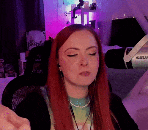 a woman with red hair is sitting in front of a shure microphone with her eyes closed