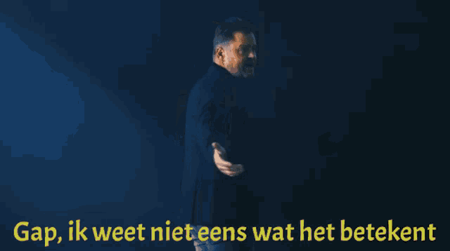 a man in a suit stands in front of a black background with gap ik weet niet eens wat het betekent written in yellow