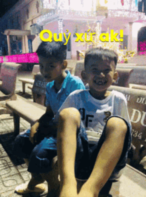 two young boys are sitting on a bench with the words quy xuak in yellow letters above them
