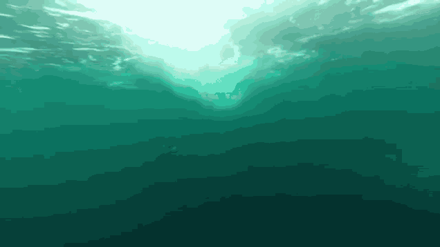 a person is swimming underwater in the ocean and the sun is shining through the water .