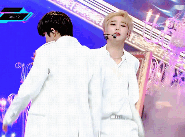 a man in a white suit is standing next to another man with a microphone in his mouth and a cloud9 logo behind him