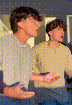 two young men are standing next to each other and one of them is wearing a cross necklace .