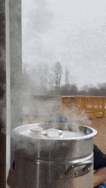 a stainless steel pot with steam coming out of it and a white lid
