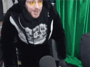 a man wearing a black hoodie with a skeleton on it stands in front of a green screen