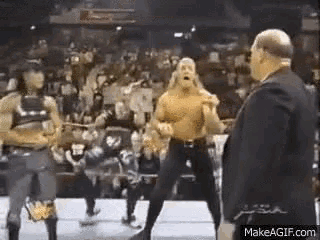 a man in a suit is standing next to a group of wrestlers in a ring .