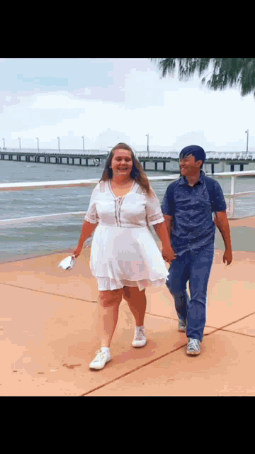 a man and a woman are holding hands while walking on a sidewalk