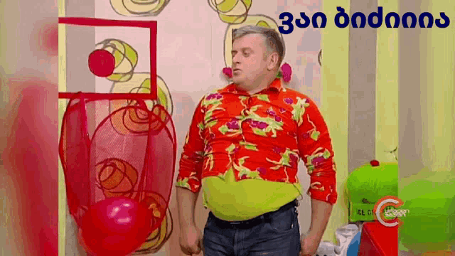 a man in a colorful shirt is standing in front of a wall with a red balloon hanging from it