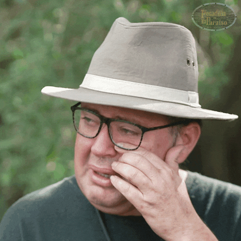 a man wearing a hat and glasses is crying in front of a sign that says paradise of the paradise