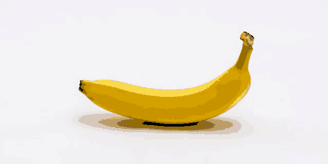 a yellow banana with a brown stem on a white surface