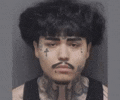 a man with a mustache and a cross tattoo on his face is looking at the camera .