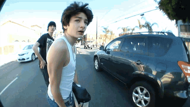 a man in a white tank top stands in front of a car that says toyota