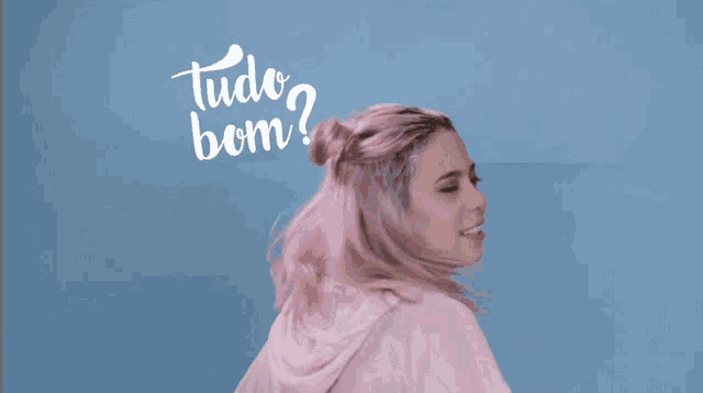 a woman with pink hair is standing in front of a blue background with the words tudo bom written on it