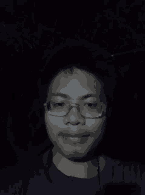 a man wearing glasses looks at the camera with a dark background