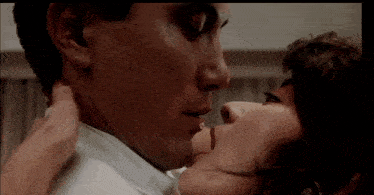 a man and a woman are kissing in a room . the woman is touching the man 's neck .