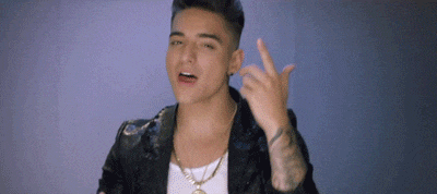 a young man wearing a leather jacket and a gold chain is making a peace sign with his finger .