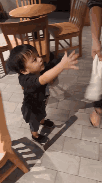 a little boy in a black shirt reaches out to someone