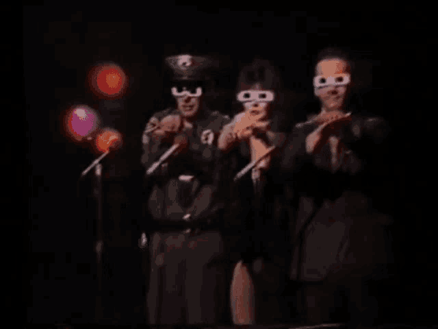 three people wearing 3d glasses are singing into microphones .