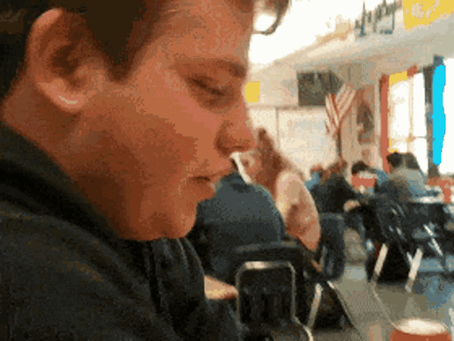 a boy sits at a table in a classroom with a flag on the wall