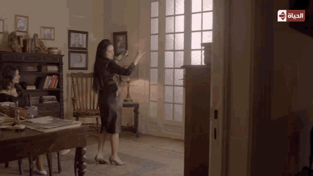 a woman in a black dress is standing in a room with arabic writing on the bottom
