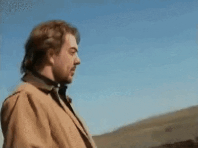 a man in a brown jacket is standing in the middle of a field .