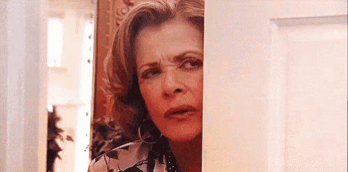 a woman is peeking out from behind a door and making a face .