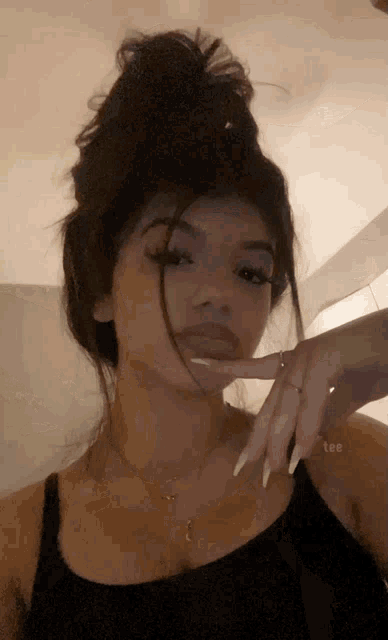 a woman with long nails and a bun is taking a selfie .