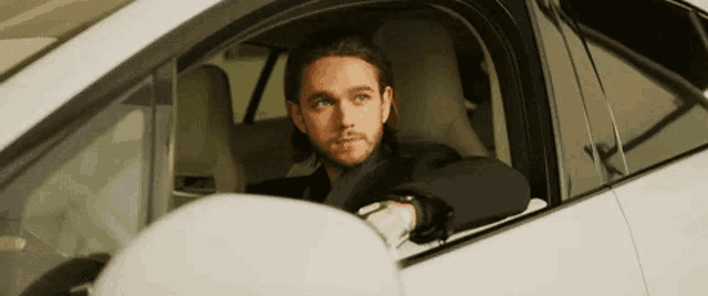 a man in a suit is sitting in the driver 's seat of a white car .