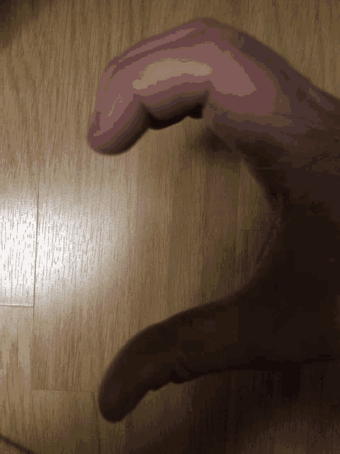 a hand is making a heart shape on a wooden surface