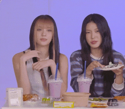 two girls are sitting at a table eating food and drinking