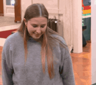 a woman wearing a gray sweater is smiling in a room .