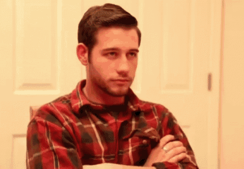 a man in a red plaid shirt is sitting with his arms crossed