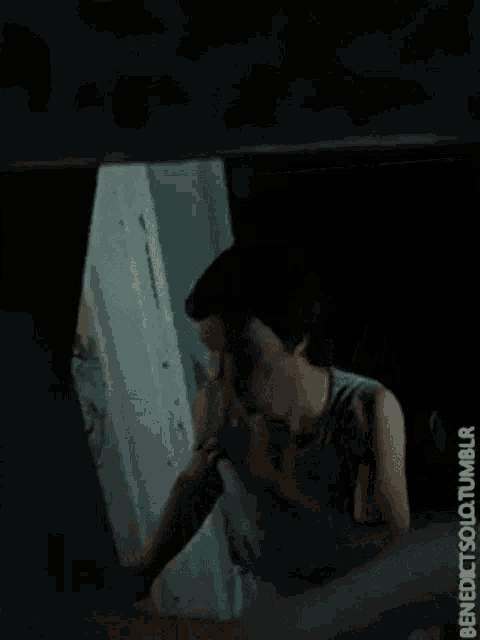 a man in a tank top is looking out of a window and smoking a cigarette ..