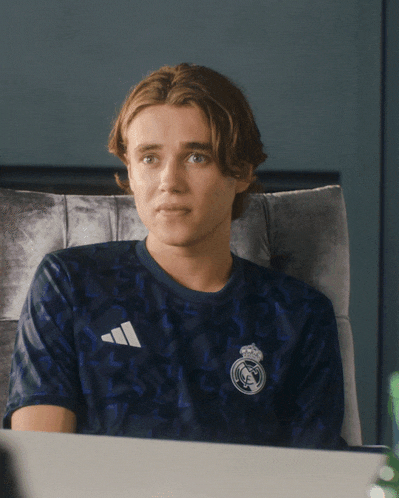 a man wearing an adidas shirt sits in a chair